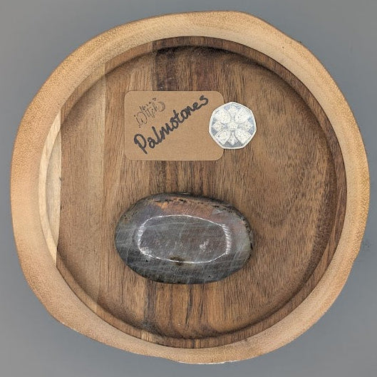 Labadorite flash palm sized stone on a wooden plate beside a 50p piece