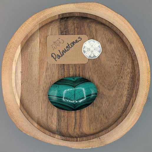 Wooden dish with a malachite stone and a silver coin on a gray background