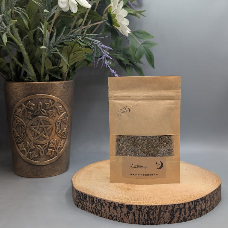Pouch of dried agrimony herb on a wooden plate with a vase and flowers behind.