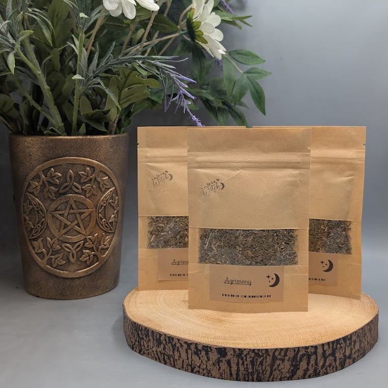 Three pouches of dried agrimony herb on a wooden plate with a vase and flowers behind.