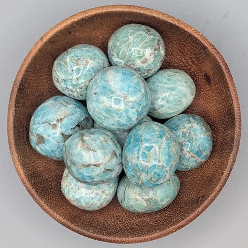 Wooden bowl filled with amazonite tumble stones on a grey background