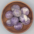 Wooden bowl filled with amethyst tumble stones on a grey background