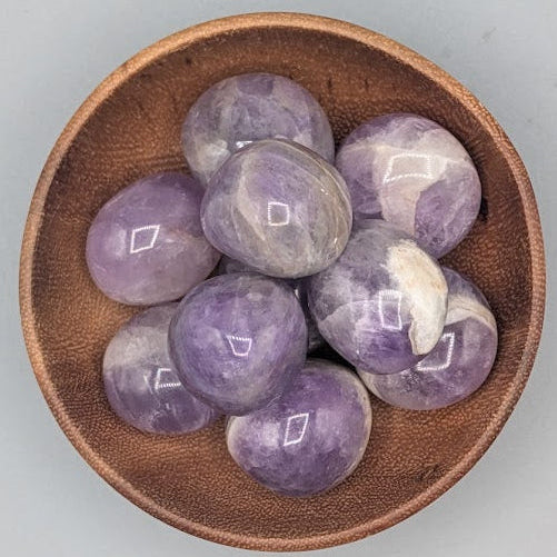Wooden bowl filled with amethyst tumble stones on a grey background