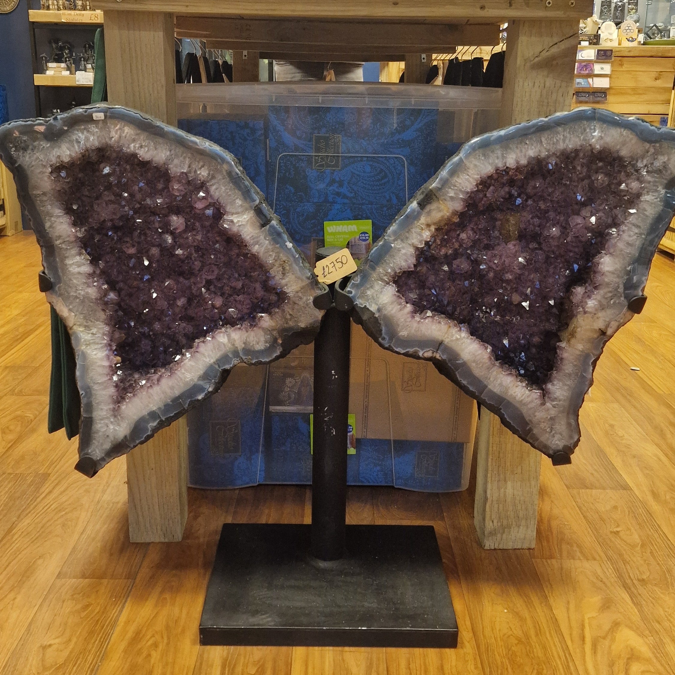 Two large amethyst geodes on a stand making the shape of wings in a store setting.