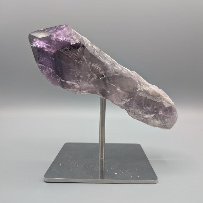Amethyst crystal on a stand against a gray background