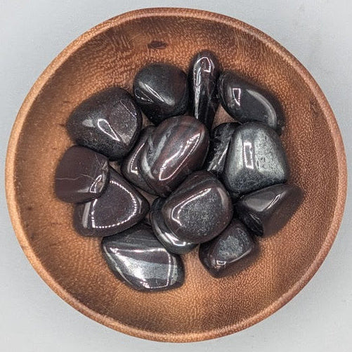 Brown bowl filled with ancestralite tumblestones on a gray background