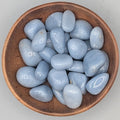 Wooden bowl filled with angelite tumble stones on a grey background
