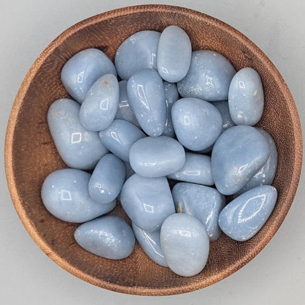Wooden bowl filled with angelite tumble stones on a grey background