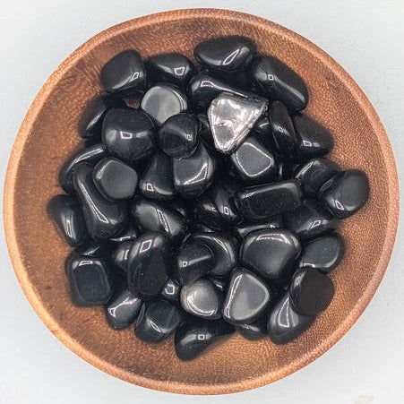 Wooden bowl filled with Apache tears tumble stones on a grey background