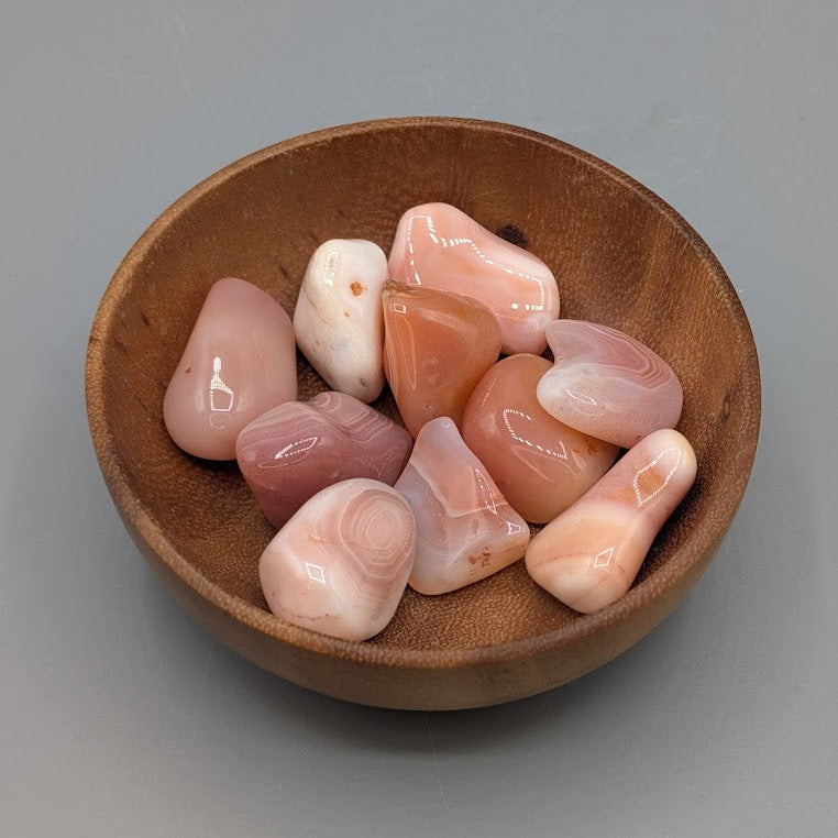Wooden bowl filled with apricot agate tumble stones on a grey background
