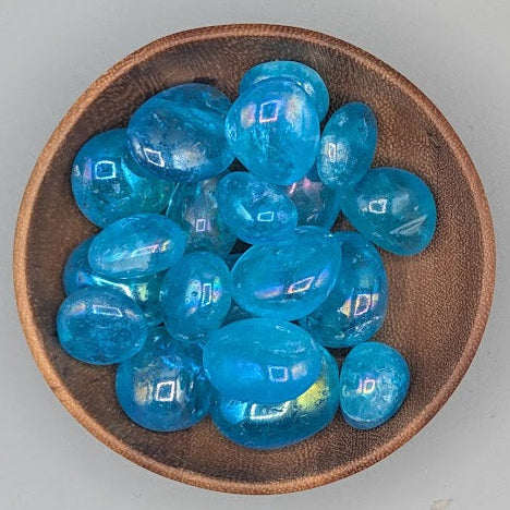 Wooden bowl filled with aqua aura quartz tumble stones on a grey background