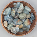 Wooden bowl filled with aquamarine tumble stones on a grey background