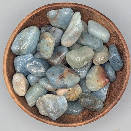 Wooden bowl filled with aquamarine tumble stones on a grey background