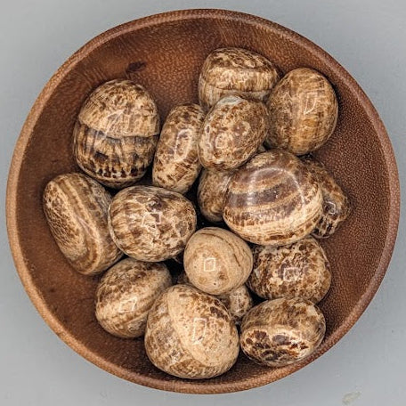 Wooden bowl filled with aragonite tumble stones on a grey background