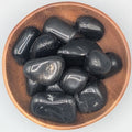 Wooden bowl filled with black agate tumble stones on a grey background