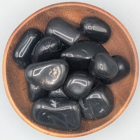 Wooden bowl filled with black agate tumble stones on a grey background