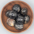 Wooden bowl filled with black moonstones tumble stones on a grey background