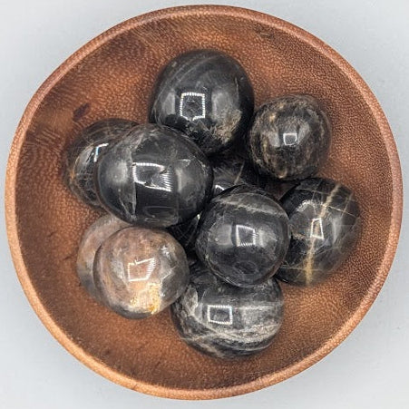 Wooden bowl filled with black moonstones tumble stones on a grey background