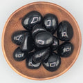 Wooden bowl filled with black obsidian tumble stones on a grey background