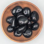 Wooden bowl filled with black obsidian tumble stones on a grey background