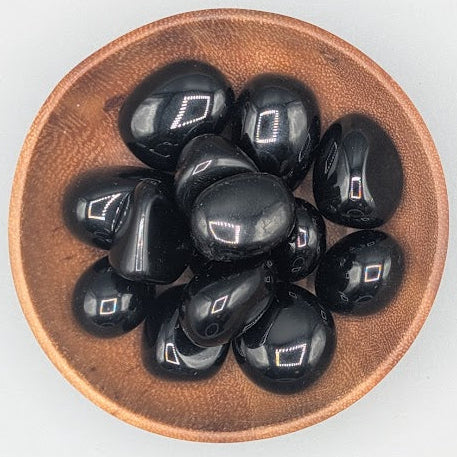 Wooden bowl filled with black obsidian tumble stones on a grey background