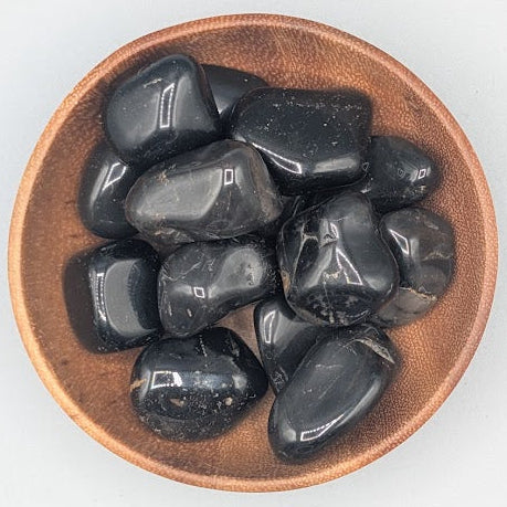 Wooden bowl filled with black onyx tumble stones on a grey background