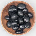 Wooden bowl filled with black tourmaline tumble stones on a grey background