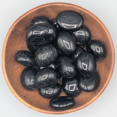Wooden bowl filled with black tourmaline tumble stones on a grey background