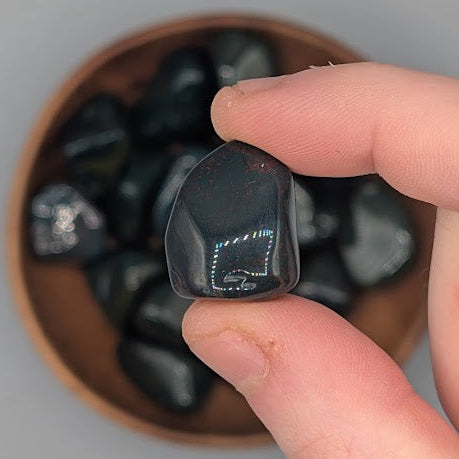 Hand holding a single bloodstone tumble with full wooden bowl of the same crystal in background