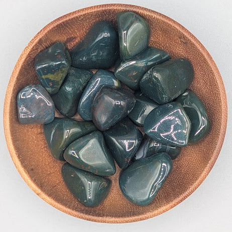 Wooden bowl filled with bloodstone tumble stones on a grey background