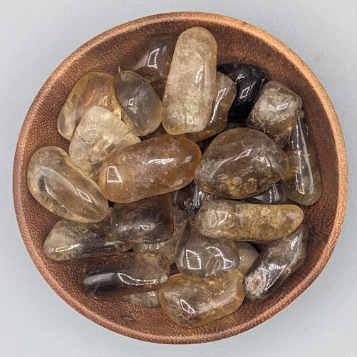 Brown bowl filled with natural citrine tumblestones on a grey background