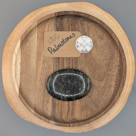 Dragons Blood Jasper palm stone on a wooden board with 50p, on a grey background