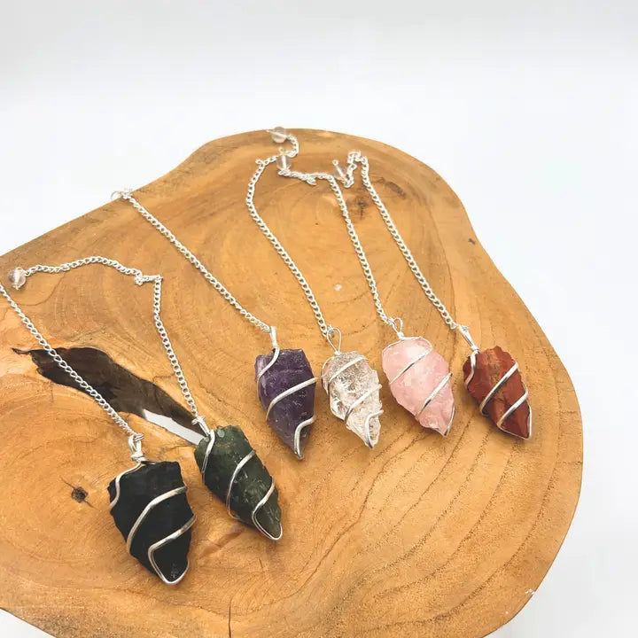 Five wire wrapped crystal pendulums on a wooden surface with a white background