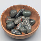 Wooden bowl filled with african bloodstone tumble stones on a grey background
