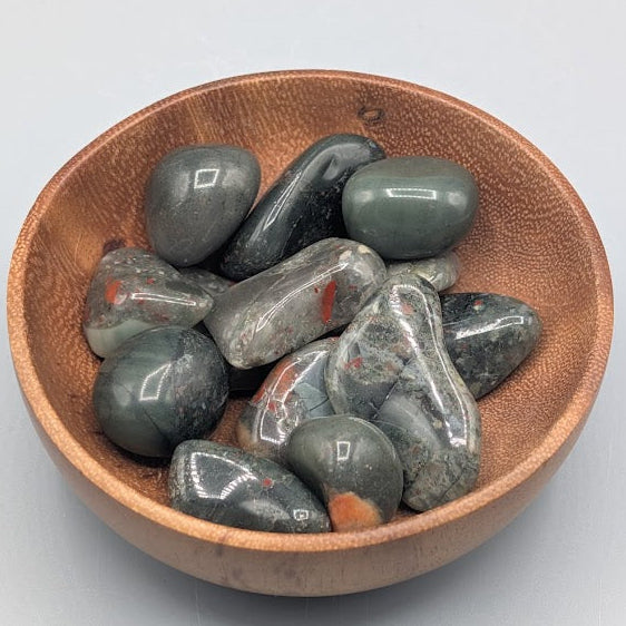 Wooden bowl filled with african bloodstone tumble stones on a grey background