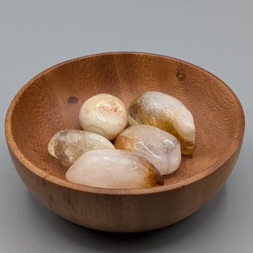 Wooden bowl filled with synthetic citrine tumble stones on a grey background